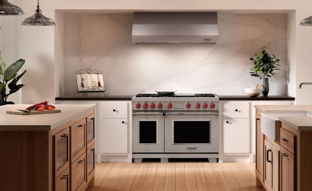 front view of a modern minimal kitchen with a wolf range in a black countertop with white cabients