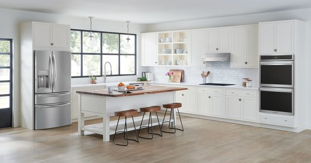 view of a modern kitchen with white counters, white walls, and stainless steel appliances