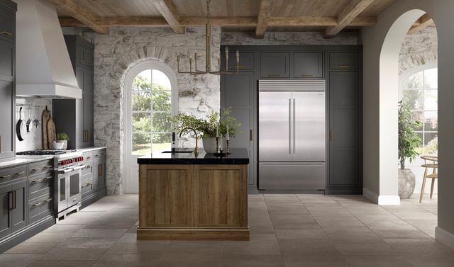 front view of a modern rustic kitchen with a stone wall, grey cabinets, and stainless steel appliances including a large 48-inch refrigerator