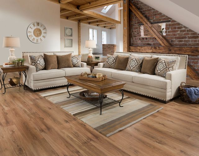 front view of a rustic living room with wood floors, white and brick walls, beige sofas, and wood tables.