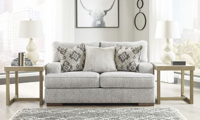 front view of a light grey loveseat with three accent pillows and a light wood side table on both sides