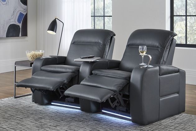 front view of two black leather theater seats with wine and popcorn in the cupholder and on the side table, respectively