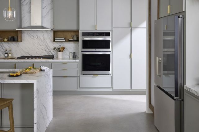 front view of a modern kitchen with a double oven, white cabinets, and a marble island and backsplash