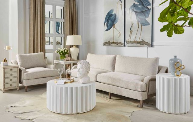 front view of a small modern living room with a cream sofa and matching chair, white drum-style coffee and side tables, all styles with modern decor