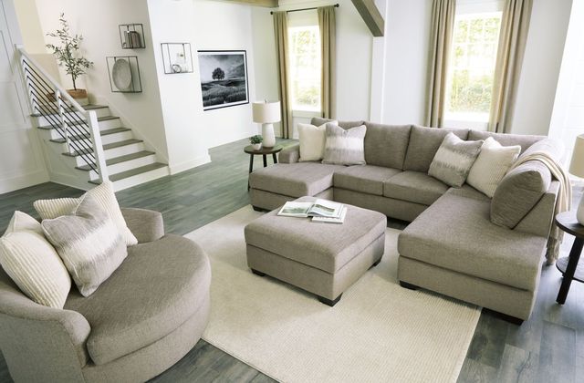 front view of a modern living room with white walls and a beige sectional with matching ottoman and oversized swivel accent chair