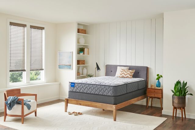 front view of a modern bedroom with white panel walls and a white rug. Centered in the room is a light wood bed frame with a gray mattress and headboard, a light wood chair, and side table.