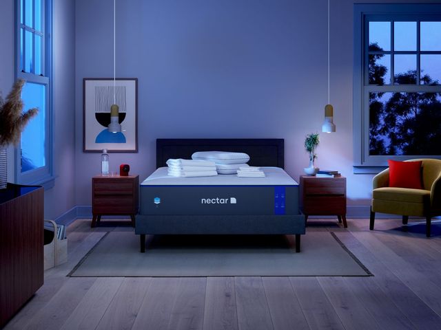 A Nectar mattress on a bedframe in a bedroom with dimmed lights