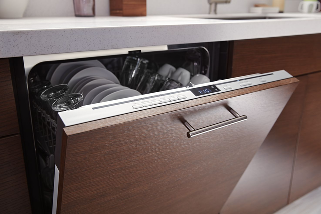 closeup view of a panel ready dishwasher with a brown wood panel slightly opened under a white countertop