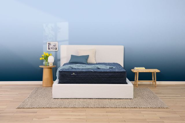 front view of a bedroom with blue walls, a white bed frame, wood side tables, and a blue mattress 