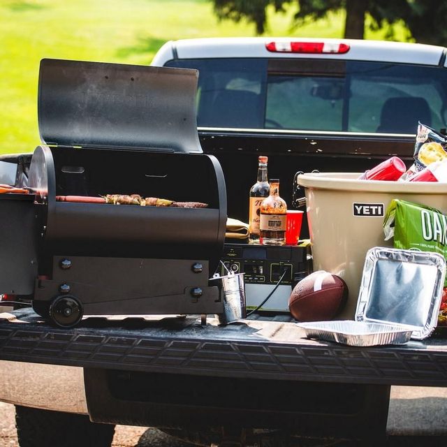 traeger grill in the back of a truck with a cooler, football, and various veggies