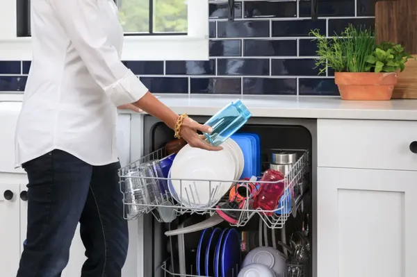 A woman is standing in front of an open dishwasher, removing clean dishes