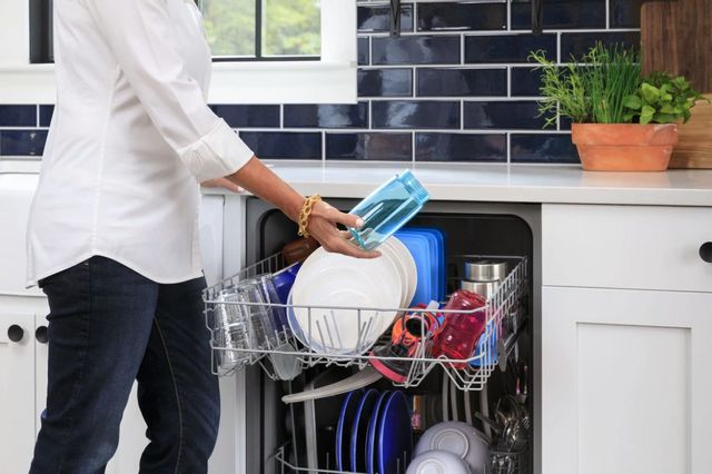 front view of a person pulling dishes out of a full dishwasher in a modern kitchen