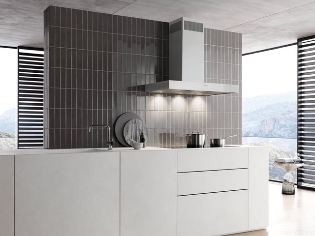 view of a wall mount range hood in a clean luxury kitchen with a black tile backsplash