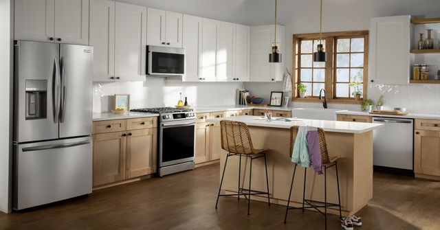 front view of a modern kitchen with light wood and white cabinetry and a stainless steel french door refrigerator and matching appliances throughout
