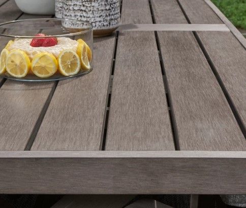 close view of a resin outdoor dining table, designed to look like wood, with a lemon cake on top