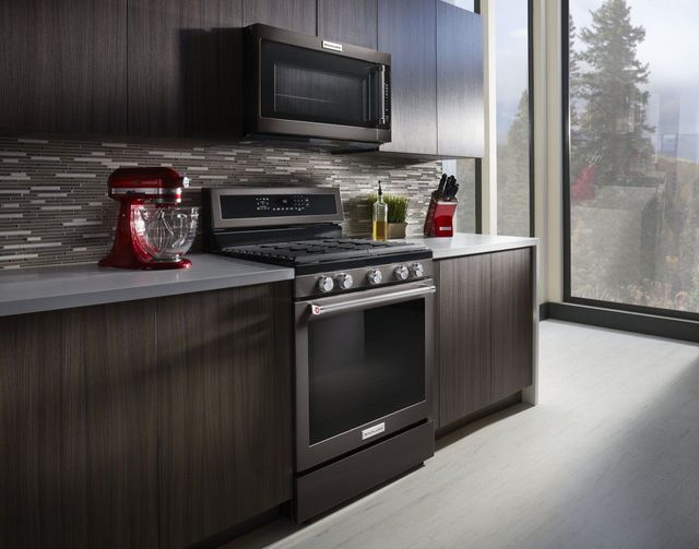 view of a modern kitchen with a kitchenaid stove, microwave, and red kitchenaid stand mixer on the counter. cabinets are dark brown and microwave and range are a black stainless finish
