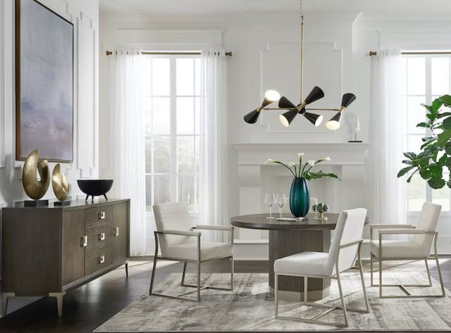 front view of a modern dining room with a round pedestal table and matching sideboard, with white upholstered seats around the table