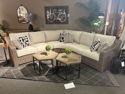 front view of the Signature Design by Ashley® Beachcroft Beige Curved 3 Piece Sectional inside a furniture showroom with accent tables, plants, and decor around