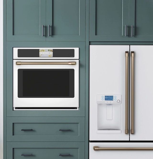 A matte white Cafe oven is installed in teal cabinetry next to a white Cafe refrigerator