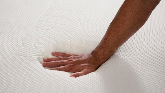 closeup view of a hand pressing onto a white purple mattress