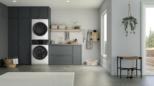 view of a modern laundry room with light grey walls, dark grey cabinetry, and a stackable washer and dryer