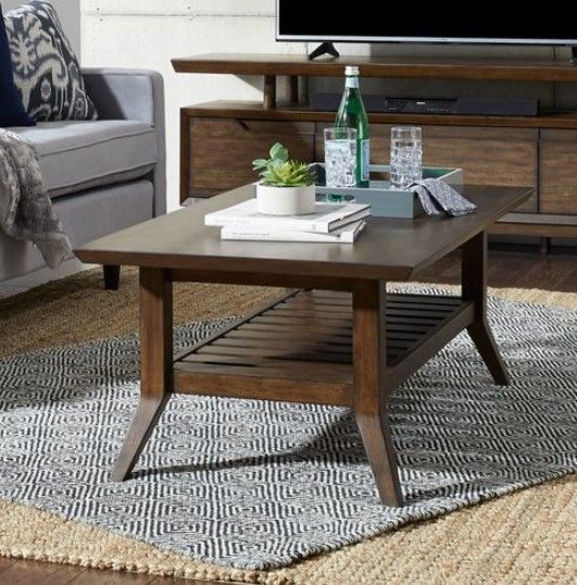 front view of a liberty furniture coffee table on top of a rug, with a matching tv stand and light blue sofa in the background