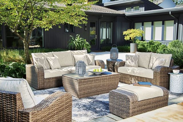 front view of an outdoor sofa, matching loveseat, chairs, and coffee table on a back deck with a house in the background