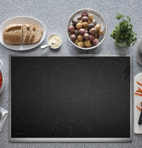 A tray of bread and a bowl of potatoes rest next to a cooktop