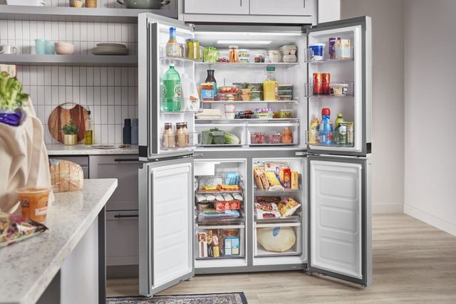 front view of a four-door refrigerator with every door open, showing a fully stocked refrigerator in a modern kitchen