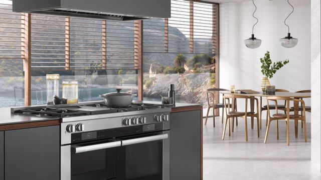 view of a luxury contemporary island and dining room with a miele range in the island, and a large glass window wall behind