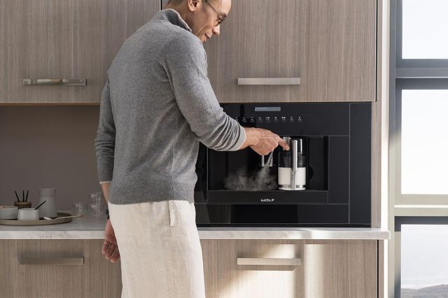 front view of a man holding a glass cut to a built in coffee maker