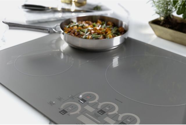 closeup view of a grey monogram cooktop with a pan of veggies cooking on the back burner