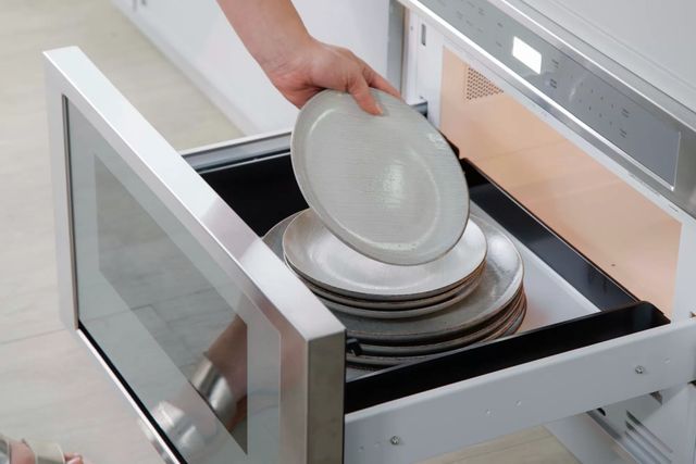 close view of an arm taking a warm plate from a stack of plates inside a pulled out microwave drawer