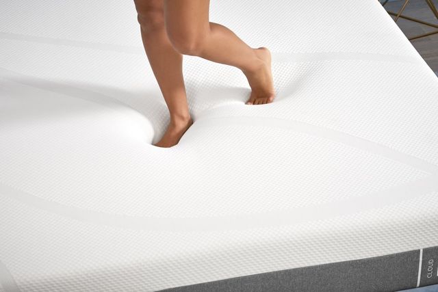 view of two legs standing on a tempur-pedic memory foam mattress
