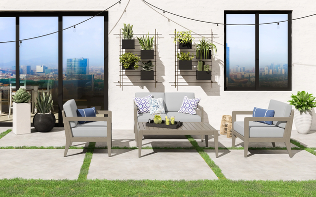 front view of a wood outdoor loveseat and matching chairs and coffee table in a modern outdoor space full of plants