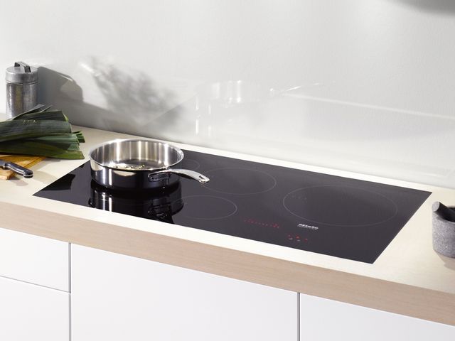 front view of a black miele induction cooktop in a white kitchen with a stainless steel pot on top