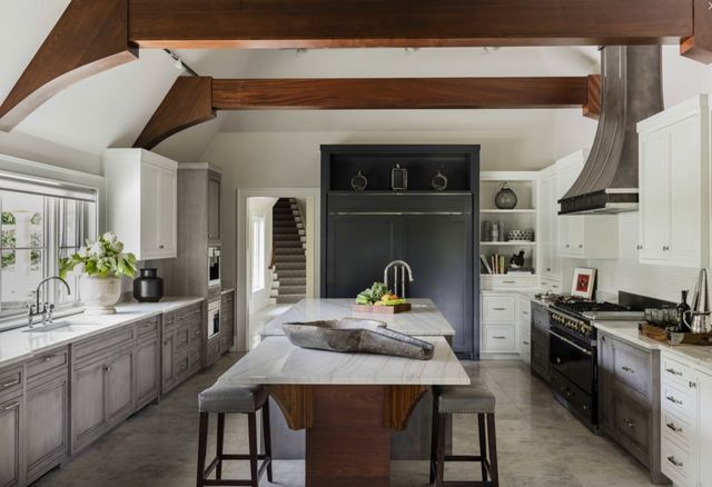 view of a modern farmhouse kitchen with white walls, black cabinets, exposed wood foundation, and a custom range hood