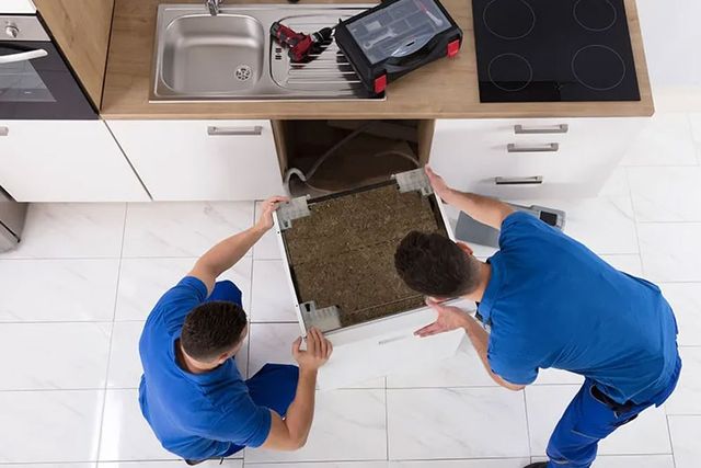top view of two men installing a built in dishwasher in a modern white kitchen